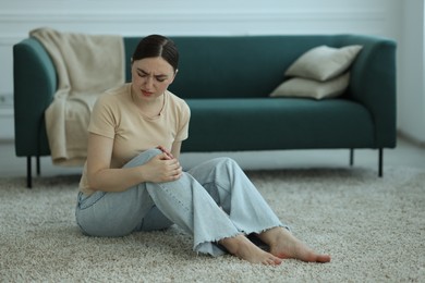 Photo of Woman suffering from knee pain on floor at home