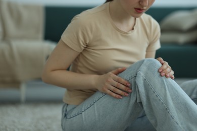 Photo of Woman suffering from knee pain on floor at home, closeup