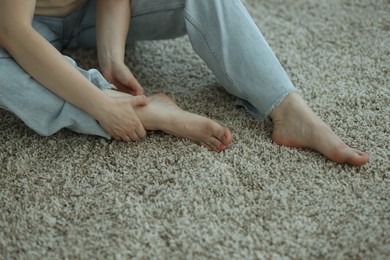 Photo of Woman suffering from foot pain on floor at home, closeup