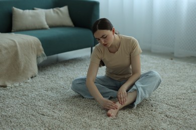 Photo of Woman suffering from foot pain on floor at home