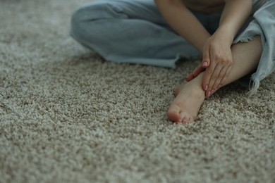 Photo of Woman suffering from foot pain on floor at home, closeup. Space for text
