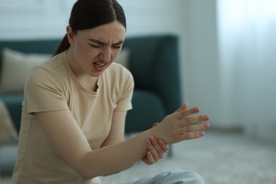 Photo of Woman suffering from wrist pain on floor at home