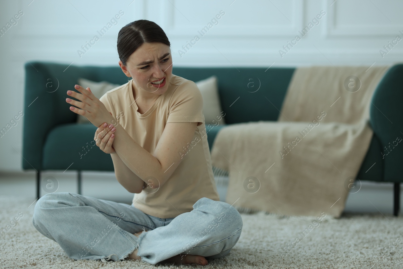 Photo of Woman suffering from wrist pain on floor at home, space for text