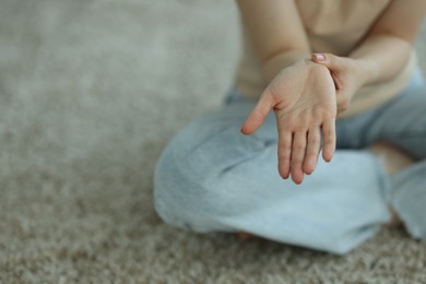 Photo of Woman suffering from wrist pain on floor at home, closeup. Space for text