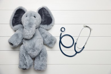 Photo of Pediatrics concept. Toy elephant with stethoscope on white wooden background, top view