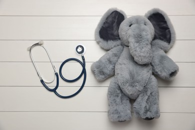 Photo of Pediatrics concept. Toy elephant with stethoscope on white wooden background, top view