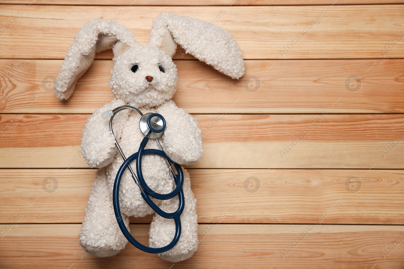 Photo of Pediatrics concept. Toy bunny with stethoscope on wooden background, top view. Space for text