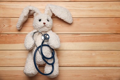 Photo of Pediatrics concept. Toy bunny with stethoscope on wooden background, top view. Space for text