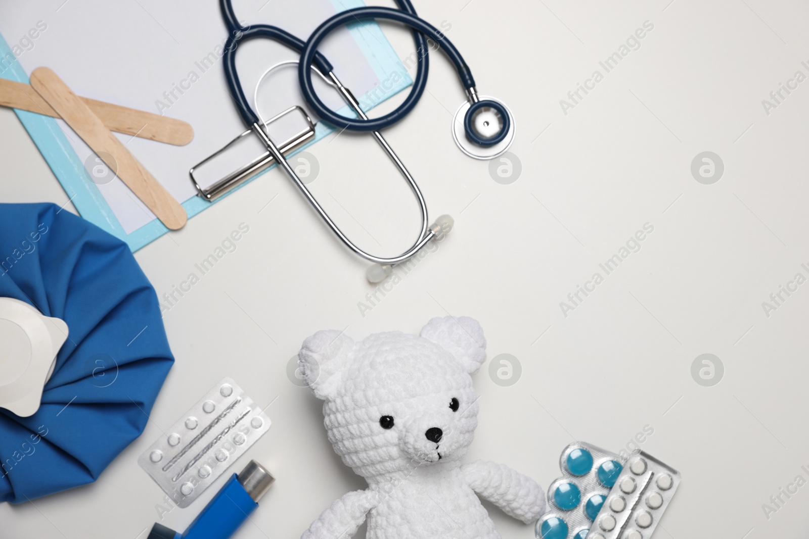 Photo of Pediatrics concept. Toy bear with stethoscope, clipboard and pills on white background, flat lay. Space for text