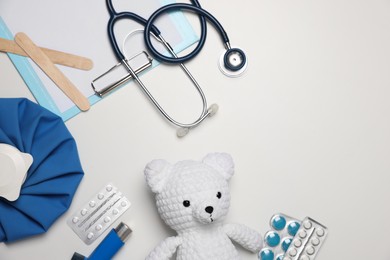 Photo of Pediatrics concept. Toy bear with stethoscope, clipboard and pills on white background, flat lay. Space for text