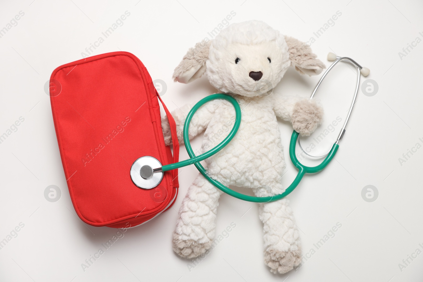 Photo of Pediatrics concept. Toy sheep with stethoscope and first aid kit on white background, top view