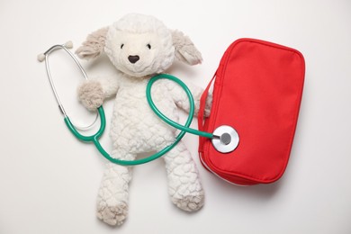 Photo of Pediatrics concept. Toy sheep with stethoscope and first aid kit on white background, top view