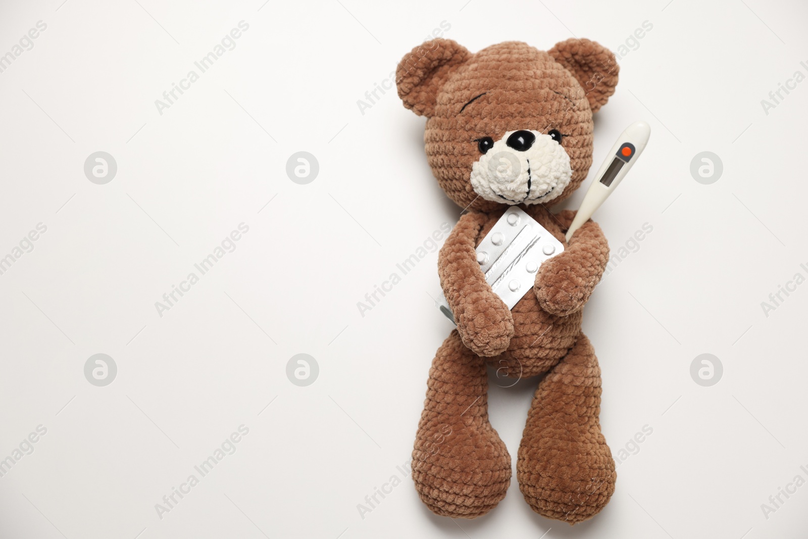 Photo of Pediatrics concept. Toy bear with thermometer and pills on white background, top view. Space for text