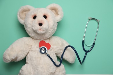 Photo of Pediatrics concept. Toy bear with stethoscope on turquoise background, top view