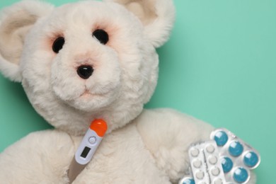 Photo of Pediatrics concept. Toy bear with thermometer and pills on turquoise background, top view