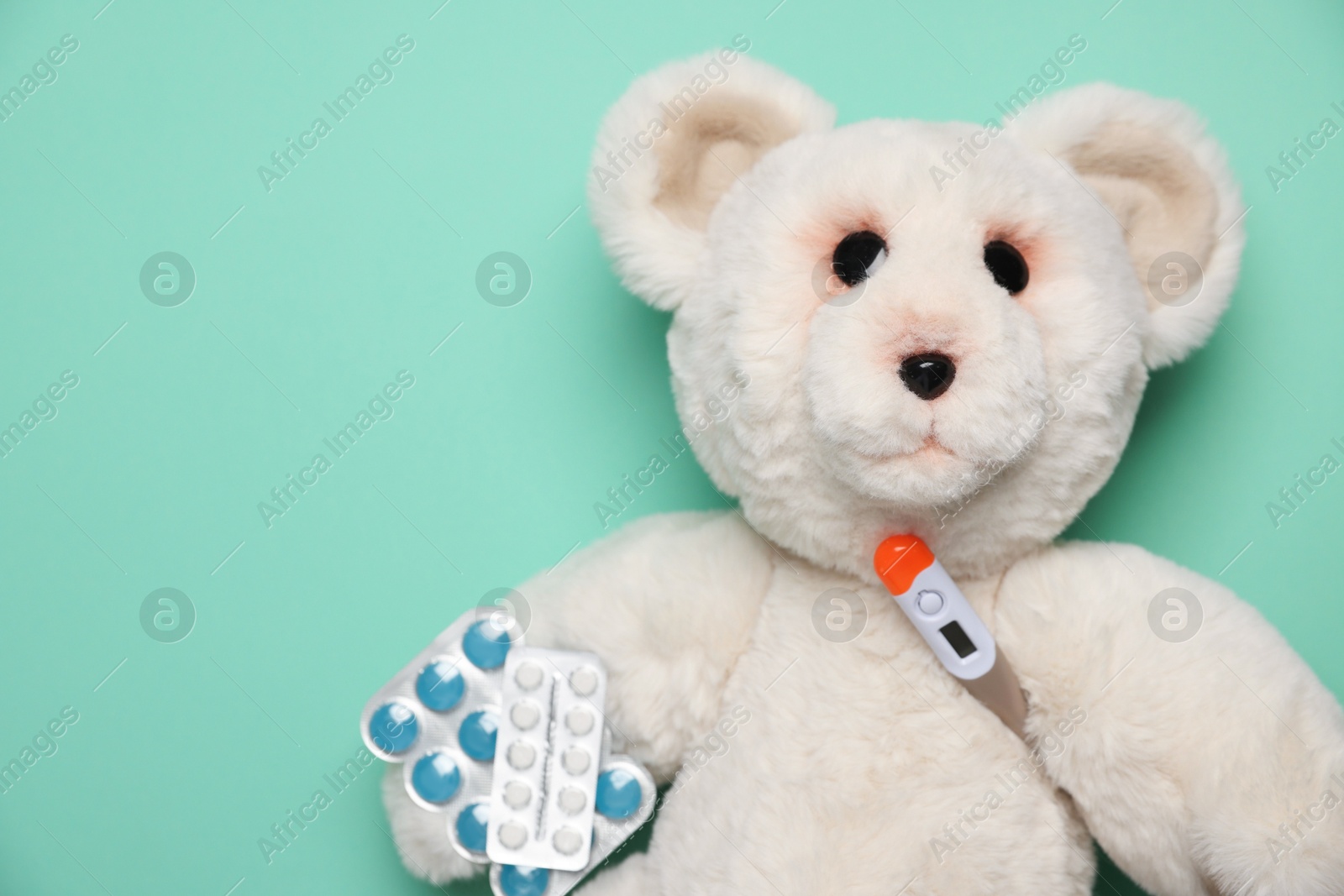 Photo of Pediatrics concept. Toy bear with thermometer and pills on turquoise background, top view. Space for text