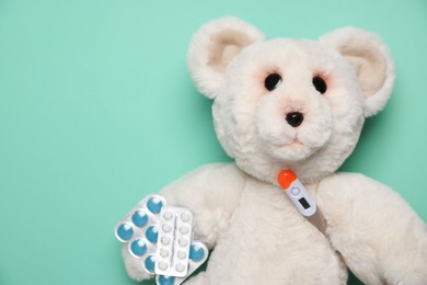 Photo of Pediatrics concept. Toy bear with thermometer and pills on turquoise background, top view. Space for text