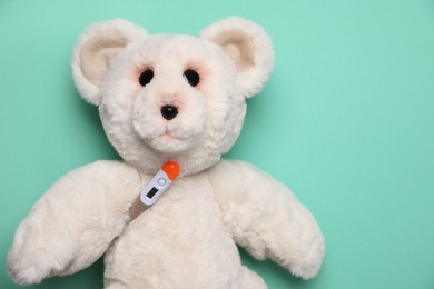 Photo of Pediatrics concept. Toy bear with thermometer on turquoise background, top view. Space for text