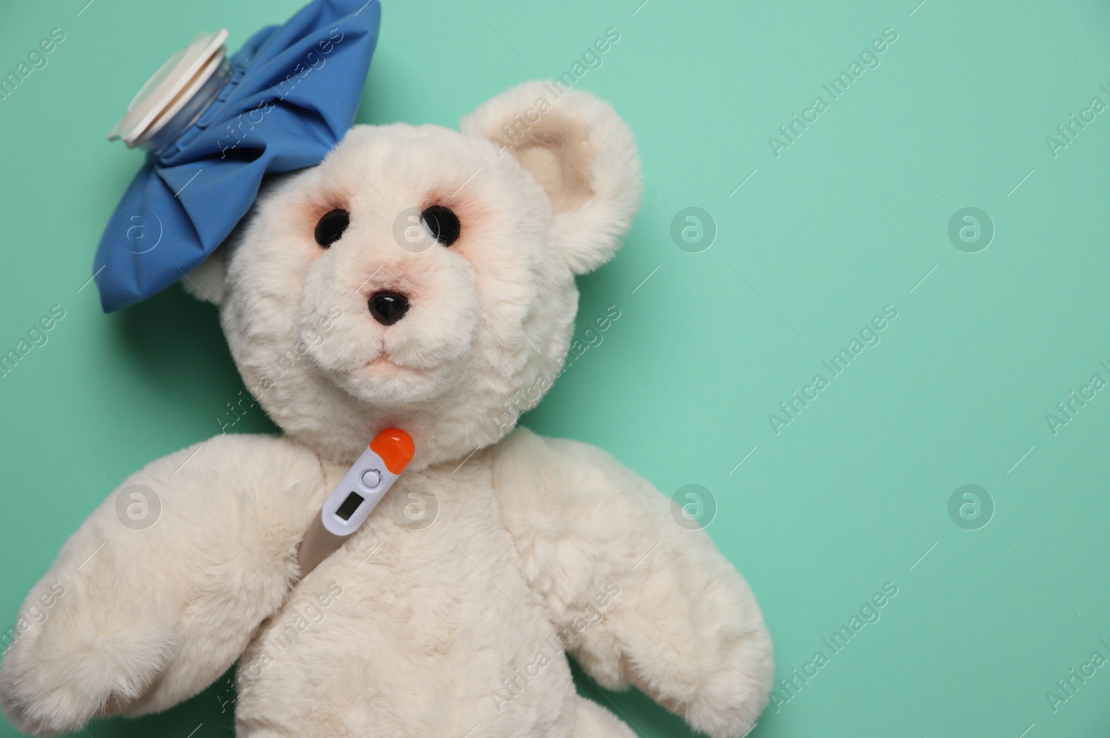 Photo of Pediatrics concept. Toy bear with thermometer and ice bag on turquoise background, top view. Space for text