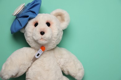 Photo of Pediatrics concept. Toy bear with thermometer and ice bag on turquoise background, top view. Space for text