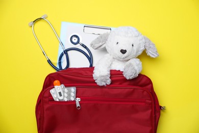 Photo of Pediatrics concept. Toy sheep with stethoscope and first aid kit on yellow background, top view