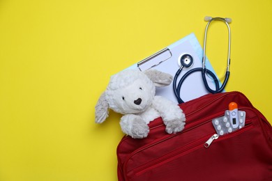 Photo of Pediatrics concept. Toy sheep with stethoscope and first aid kit on yellow background, top view. Space for text