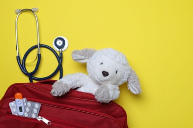Photo of Pediatrics concept. Toy sheep with stethoscope and first aid kit on yellow background, top view. Space for text