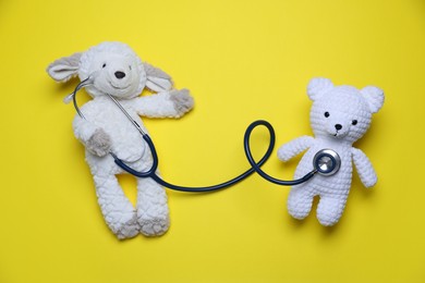 Photo of Pediatrics concept. Toy sheep and bear with stethoscope on yellow background, top view