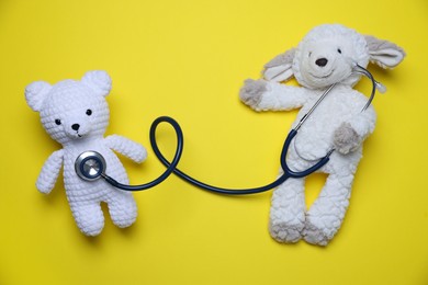 Photo of Pediatrics concept. Toy sheep and bear with stethoscope on yellow background, top view