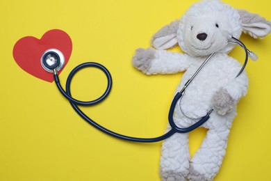 Photo of Pediatrics concept. Toy sheep with stethoscope on yellow background, top view