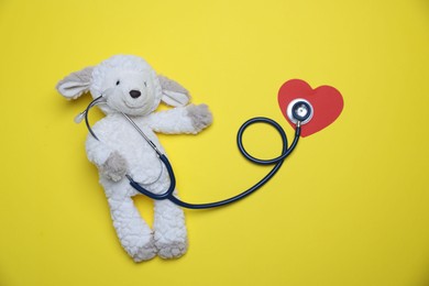Photo of Pediatrics concept. Toy sheep with stethoscope on yellow background, top view
