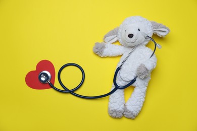 Photo of Pediatrics concept. Toy sheep with stethoscope on yellow background, top view