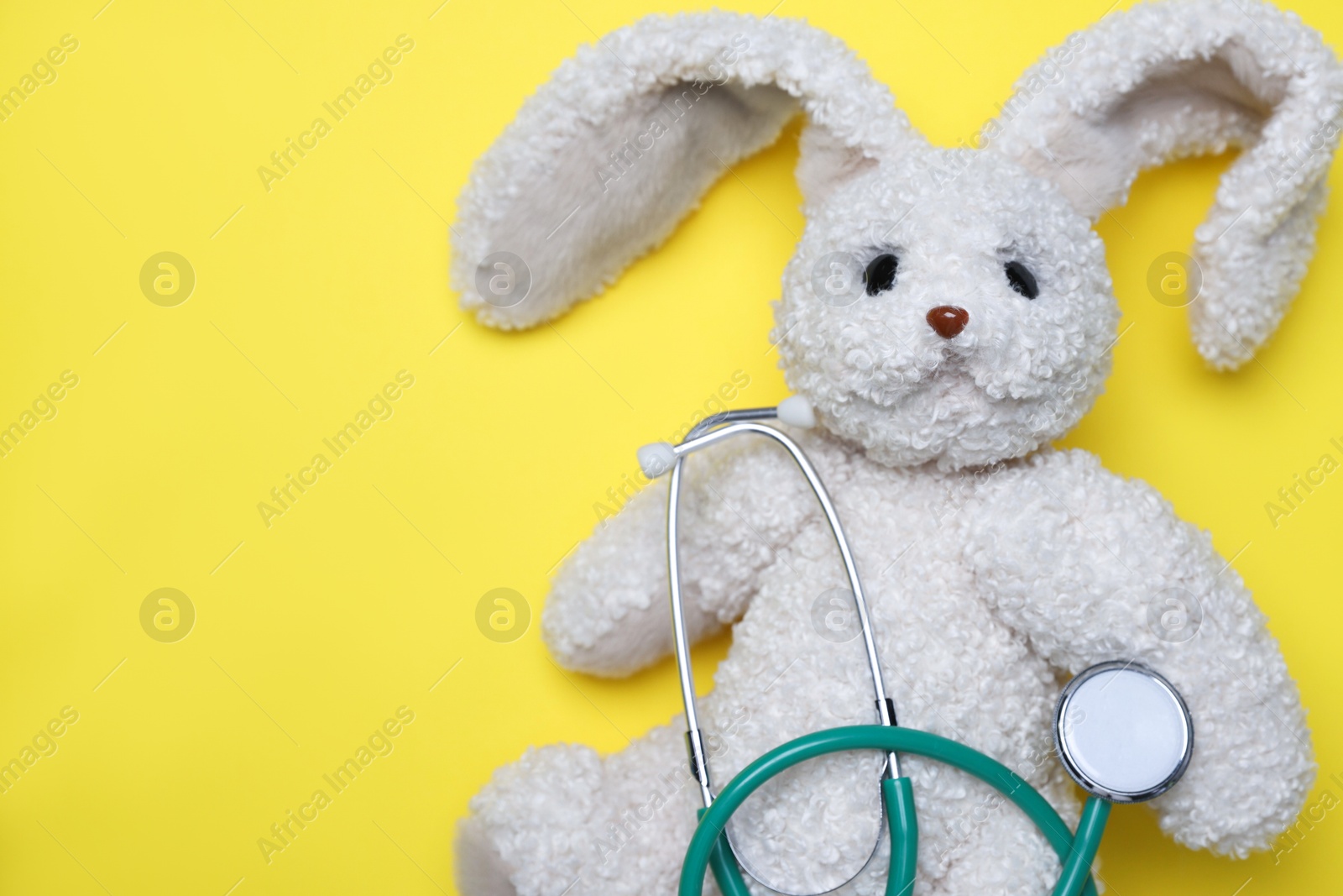 Photo of Pediatrics concept. Toy bunny with stethoscope on yellow background, top view. Space for text