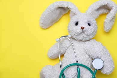 Photo of Pediatrics concept. Toy bunny with stethoscope on yellow background, top view. Space for text