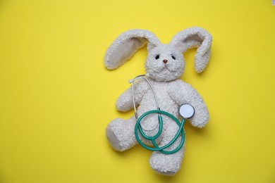 Photo of Pediatrics concept. Toy bunny with stethoscope on yellow background, top view. Space for text
