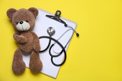 Photo of Pediatrics concept. Toy bear with stethoscope and clipboard on yellow background, top view. Space for text