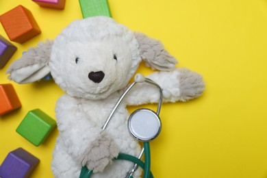 Photo of Pediatrics concept. Toy sheep with stethoscope and cubes on yellow background, top view