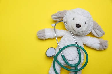 Photo of Pediatrics concept. Toy sheep with stethoscope on yellow background, top view. Space for text
