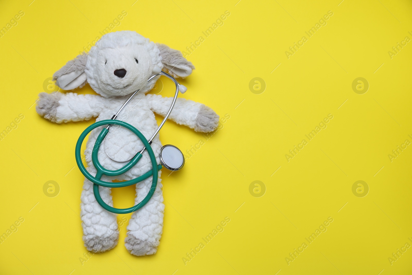 Photo of Pediatrics concept. Toy sheep with stethoscope on yellow background, top view. Space for text
