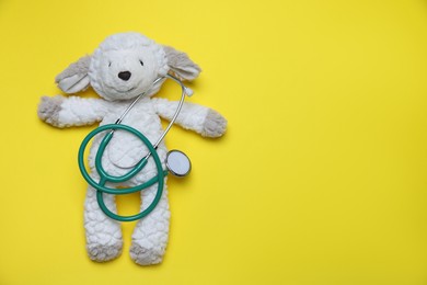 Photo of Pediatrics concept. Toy sheep with stethoscope on yellow background, top view. Space for text
