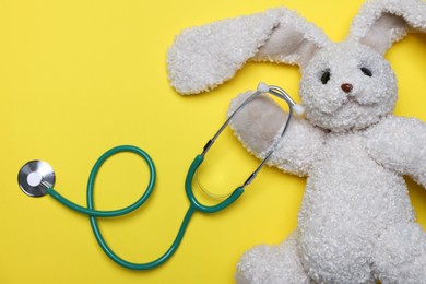 Photo of Pediatrics concept. Toy bunny with stethoscope on yellow background, top view