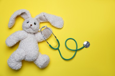 Photo of Pediatrics concept. Toy bunny with stethoscope on yellow background, top view