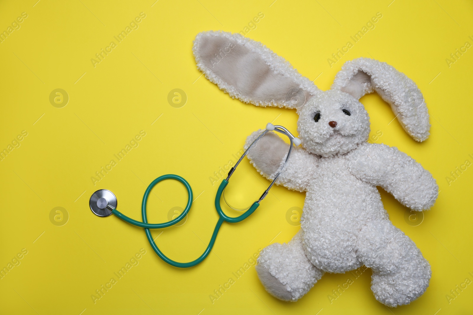 Photo of Pediatrics concept. Toy bunny with stethoscope on yellow background, top view