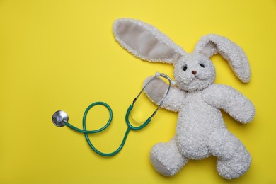 Photo of Pediatrics concept. Toy bunny with stethoscope on yellow background, top view