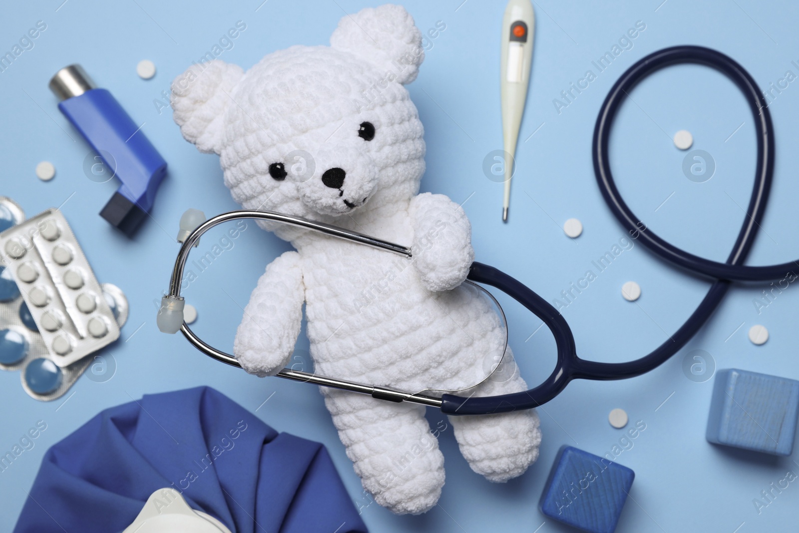 Photo of Pediatrics concept. Toy bear with stethoscope, thermometer and pills on light blue background, flat lay