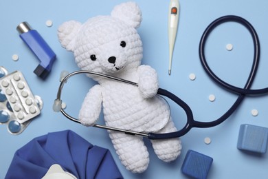 Photo of Pediatrics concept. Toy bear with stethoscope, thermometer and pills on light blue background, flat lay