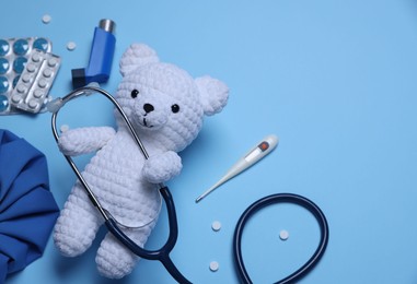 Photo of Pediatrics concept. Toy bear with stethoscope, thermometer and pills on light blue background, flat lay