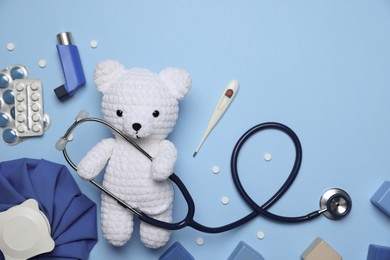 Photo of Pediatrics concept. Toy bear with stethoscope, thermometer and pills on light blue background, flat lay