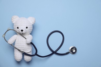 Photo of Pediatrics concept. Toy bear with stethoscope on light blue background, top view. Space for text