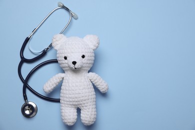 Photo of Pediatrics concept. Toy bear with stethoscope on light blue background, top view. Space for text